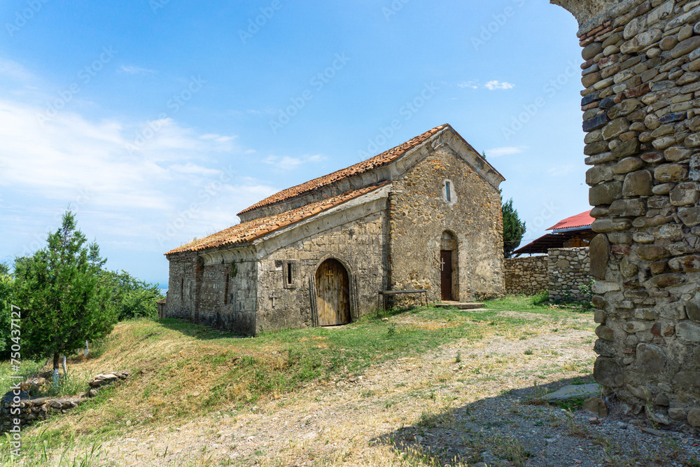 Old stone church with orange tiled roof. Stone wall and wooden door with a cross. Bright blue sky with clouds. Old stone church with orange tiled roof. Stone wall and wooden door with a cross. Bright blue sky with clouds.
