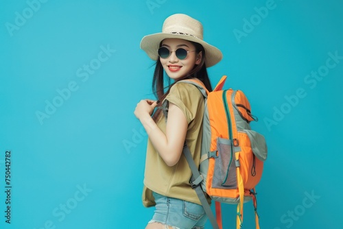 Happy young Asian tourist woman wearing beach hat, sunglasses and backpacks going to travel on holidays on blue background. © Straxer