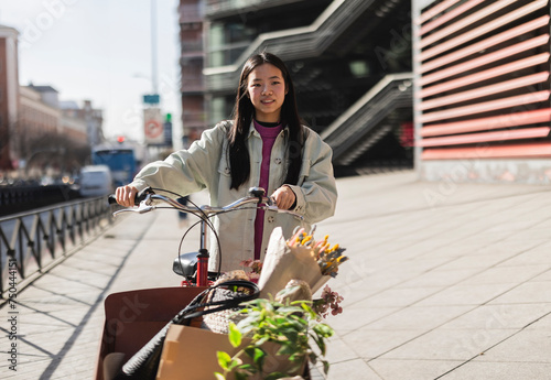 Smiling young woman walking on footpath with cargo bike photo