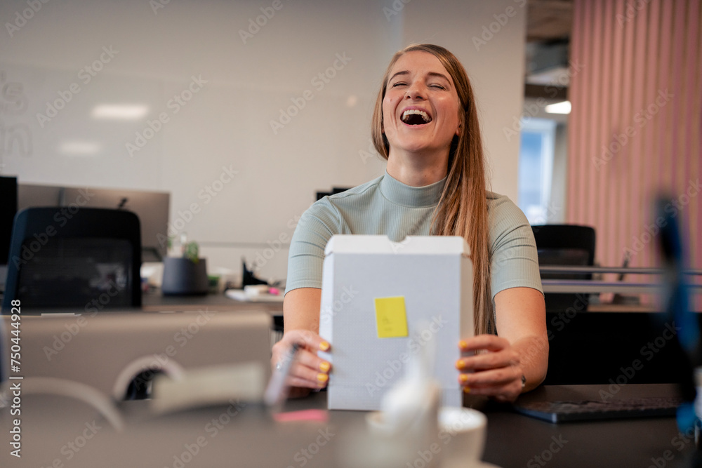 Cheerful businesswoman opening package at desk in office Cheerful businesswoman opening package at desk in office