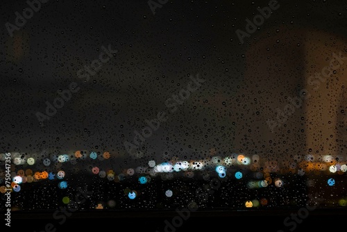 Finestra bagnata dalle gocce di pioggia con sfondo luci della città sfocate photo