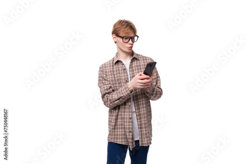 young joyful red-haired guy with glasses in a plaid shirt writes a message on the phone