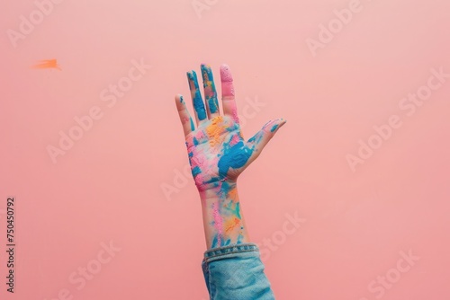 A woman s hand raised against a pink background  splattered with vibrant blue and pink paint