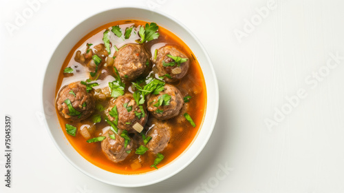 Meatball soup in a bowl garnished with fresh herbs, top view isolated on white background. Comfort food concept