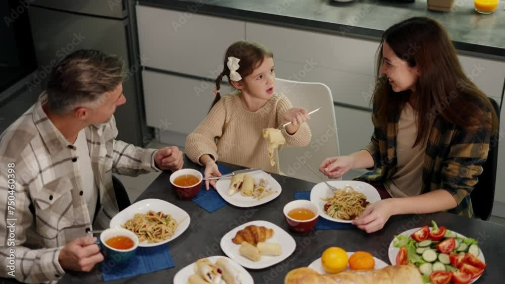 Top view of a happy family having dinner together at the table in the kitchen in the evening. Happy little girl with her brunette mom in a plaid shirt and middle-aged dad and gray hair having dinner Top view of a happy family having dinner together at the table in the kitchen in the evening. Happy little girl with her brunette mom in a plaid shirt and middle-aged dad and gray hair having dinner