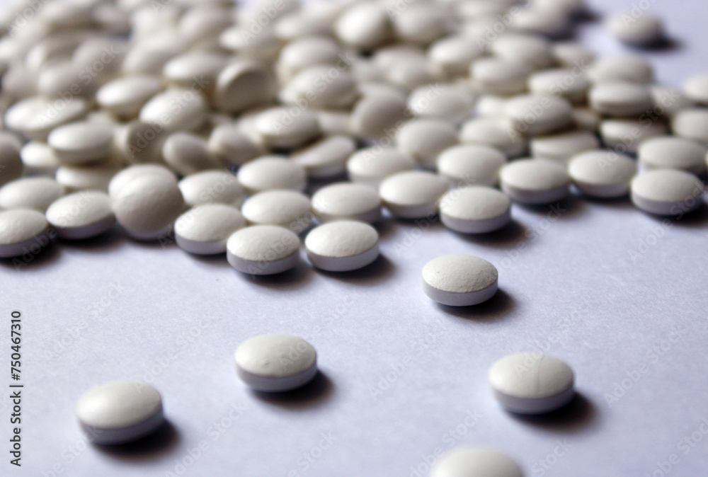 A lot of white pills are scattered on a white background. A lot of white pills are scattered on a white background.