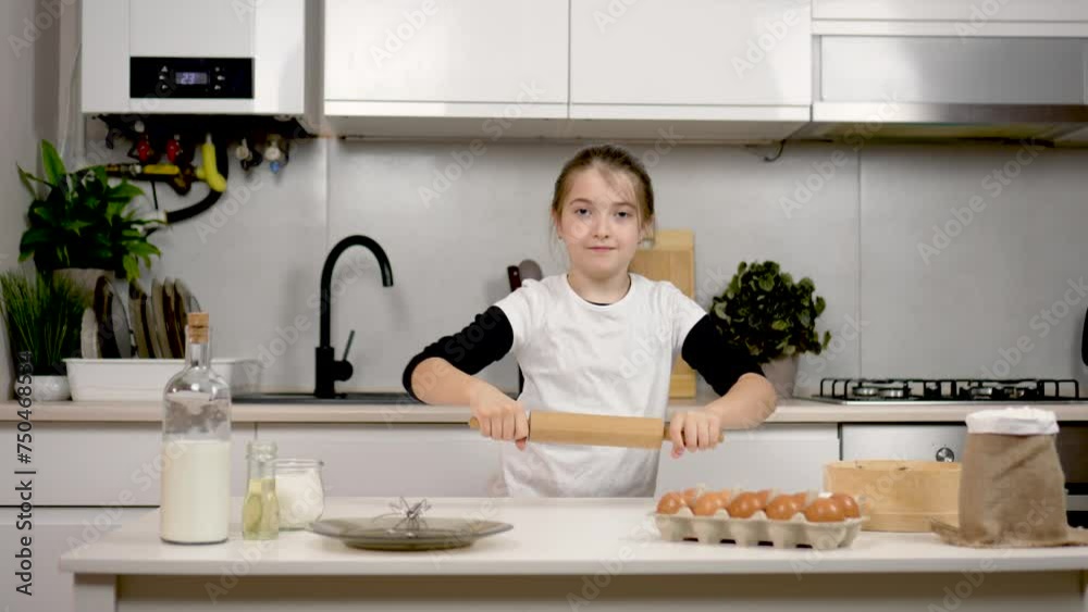 Beautiful sweet little girl dancing funny dance with rolling pin in hands in cozy kitchen. Simulates swing of dough. Ingredients eggs milk and flour nearby. Happy daughter preparing pancakes or Beautiful sweet little girl dancing funny dance with rolling pin in hands in cozy kitchen. Simulates swing of dough. Ingredients eggs milk and flour nearby. Happy daughter preparing pancakes or