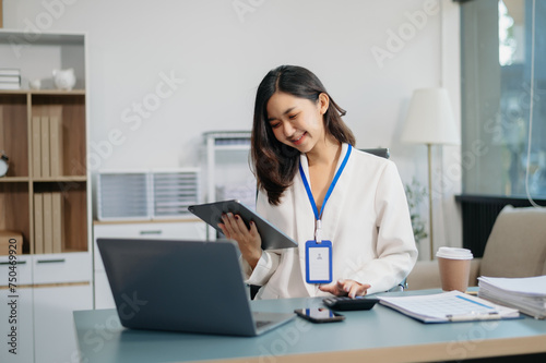 Young beautiful woman typing on tablet and laptop while sitting at the working white table