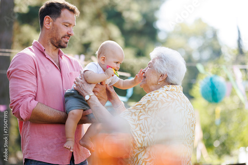 Great-grandmother holding little baby in her arms. Family summer garden party.