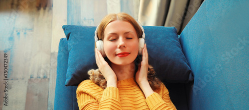 Happy relaxed young woman listening to music with headphones lies on couch at home © rohappy