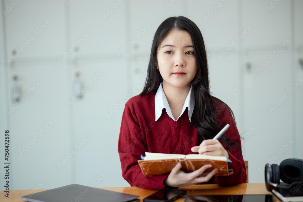 Happy young asian woman wearing earphones and using laptop computer at desk in office, Female student with stack of books and laptop. Happy young asian woman wearing earphones and using laptop computer at desk in office, Female student with stack of books and laptop.