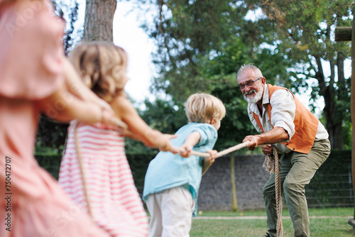 Grandfather has a tug of war with their grandkids. Fun games at family garden party.