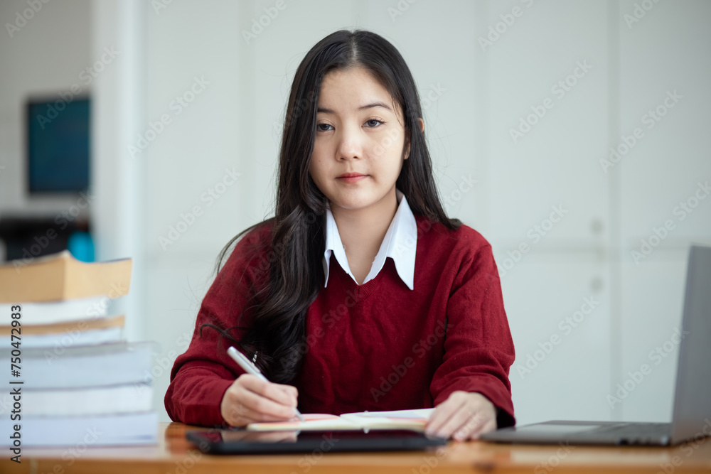Happy young asian woman wearing earphones and using laptop computer at desk in office, Female student with stack of books and laptop. Happy young asian woman wearing earphones and using laptop computer at desk in office, Female student with stack of books and laptop.