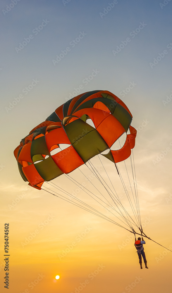 Obraz premium Parasailing extreme sports on beach in blue sky background. Man is parasailing in the blue sky. Paragliding in the clear sky above the sea.
