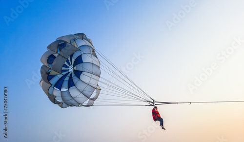 Parasailing extreme sports on beach in blue sky background. Man is parasailing in the blue sky. Paragliding in the clear sky above the sea.