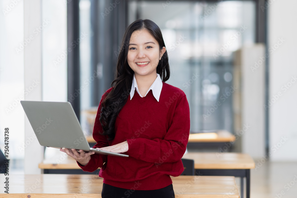 Happy young asian woman holding a laptop computer at desk in office. Happy young asian woman holding a laptop computer at desk in office.