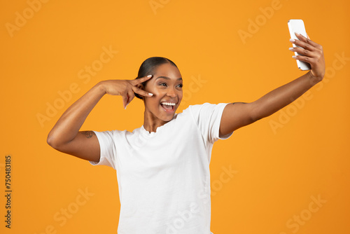 Happy African American woman making selfie with smartphone, yellow background