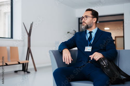 Pharmaceutical sales representative sitting in medical building, waiting for doctor, presenting new pharmaceutical product. Drug rep sitting in hall holding smartphone.