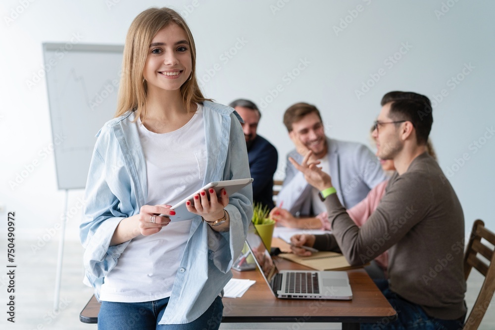 Successful young woman standing in front of businesspeople and smiling. Portrait of confident and proud businesswoman with team working in background at modern office