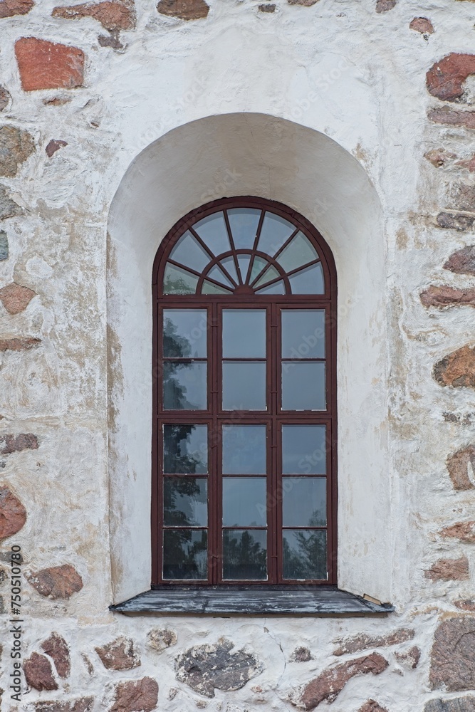 Brown painted wood frames on a window with arch on a stone building. Brown painted wood frames on a window with arch on a stone building.