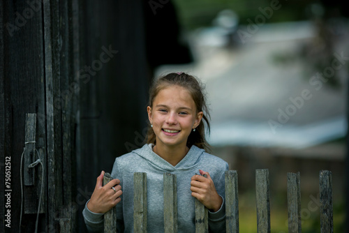A teenage girl stands by a wooden hedge on a farm.