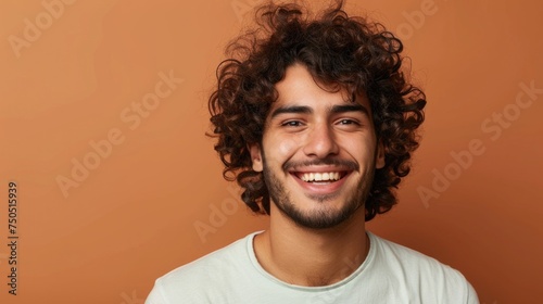 portrait of a man, Portrait of merry positive curly haired Hindu man smiles pleasantly being in good mood dressed in casual t shirt looks directly at camera isolated over brown background.  © suphakphen