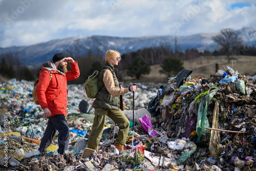 Couple of hikers walking across landfill, large pile of waste, environmental concept and eco activism.