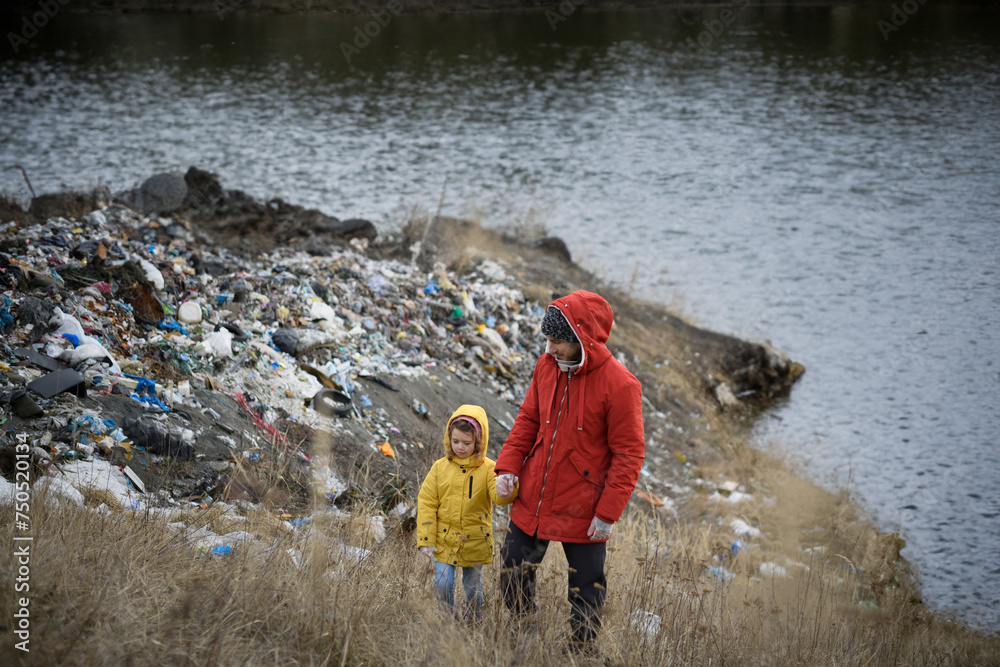 Little girl with father standing on river shore looking at piles of waste, debris on riverbank. Water and environmental pollution, eco activism concept. Little girl with father standing on river shore looking at piles of waste, debris on riverbank. Water and environmental pollution, eco activism concept.