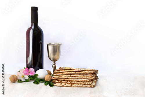 Matzo, wine, silver bowl, pink flowers apple tree, white egg and walnuts for passover celebration on white wooden table on light background with space for text