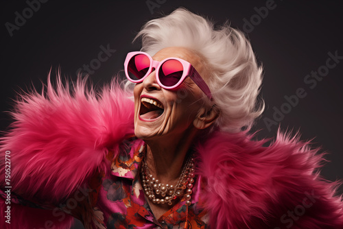 Stylish elderly woman in pink fur with sunglasses in a studio on a plain background