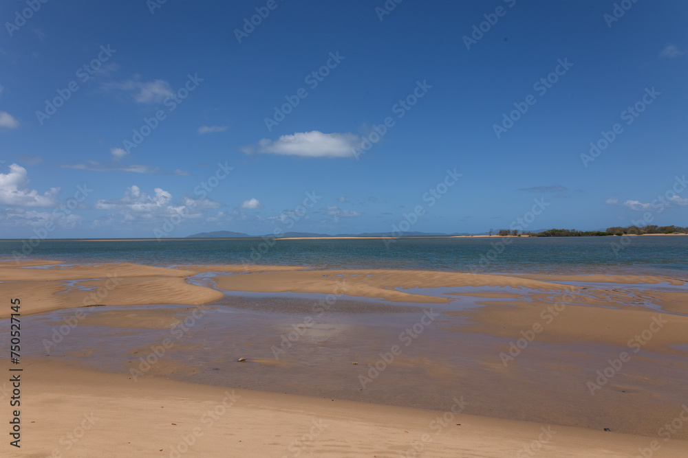 A landscape of a tropical beach at low tide with an offshore spit and exposed sand banks and blue sky with clouds at Taylor's Beach near Cardwell in Queensland, Australia
