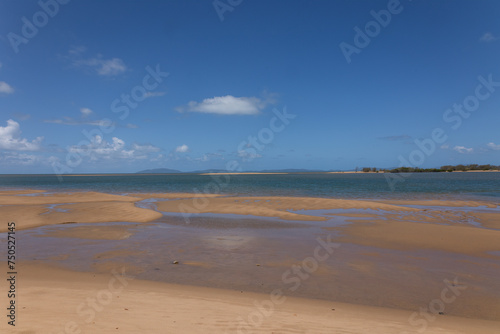 A landscape of a tropical beach at low tide with an offshore spit and exposed sand banks and blue sky with clouds at Taylor's Beach near Cardwell in Queensland, Australia