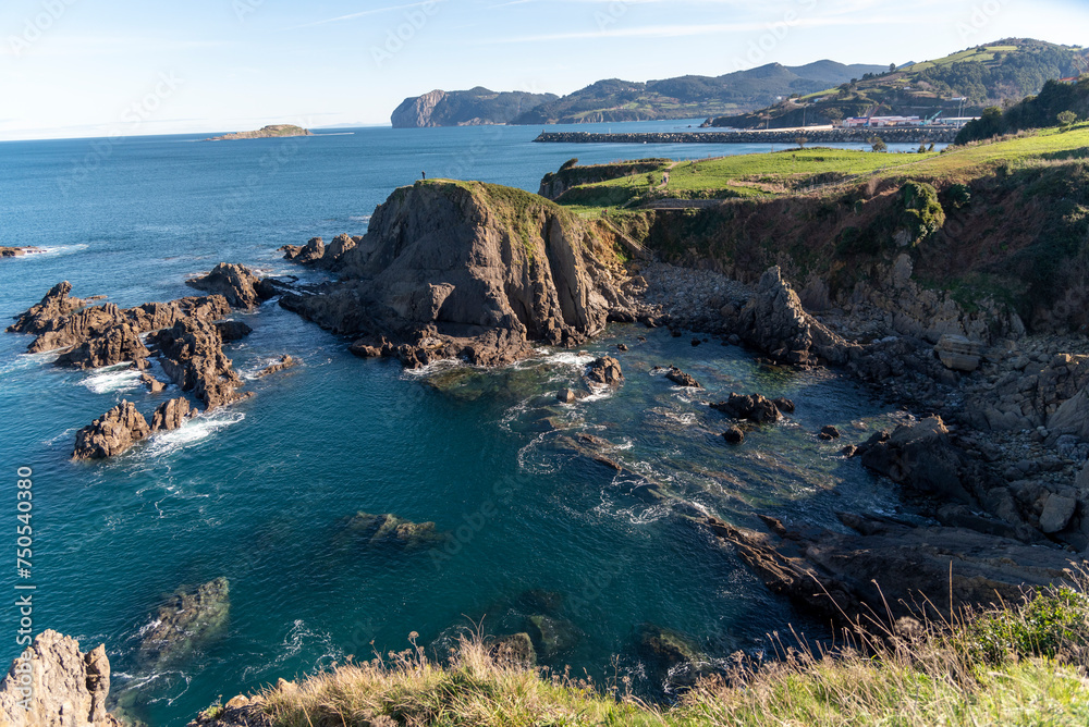 Obraz premium Panoramic view of the Basque coastal landscape of cliffs, calm sea and green vegetation on a sunny day with clear sky
