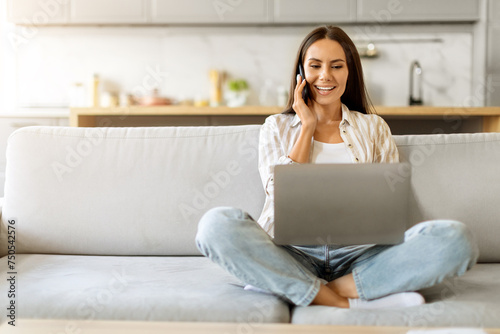 Remote Business. Young Woman Talking On Phone And Using Laptop At Home