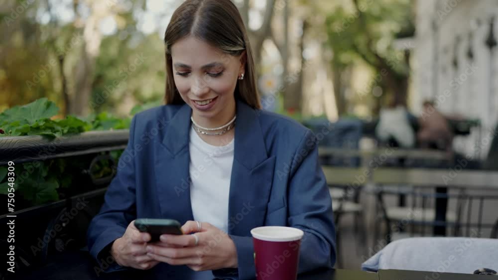 Stylish pretty woman sitting at cafe table outdoors and chatting online using smartphone. Attractive female scrolling social media on mobile phone and smile during coffee break at restaurant Stylish pretty woman sitting at cafe table outdoors and chatting online using smartphone. Attractive female scrolling social media on mobile phone and smile during coffee break at restaurant