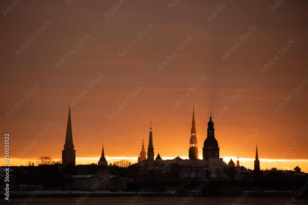 A beautiful, colorful sunrise landscape with city centre building silhouette against bright morning sky. A winter lansdcape with frozen river Daugava in Latvia capital Riga.