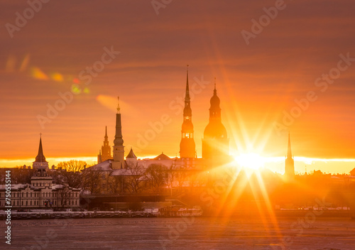 A beautiful, colorful sunrise landscape with city centre building silhouette against bright morning sky. A winter lansdcape with frozen river Daugava in Latvia capital Riga.