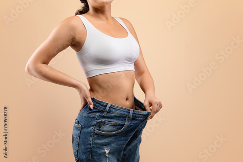 Fit woman confidently demonstrating successful weight loss by pulling out oversized jeans,