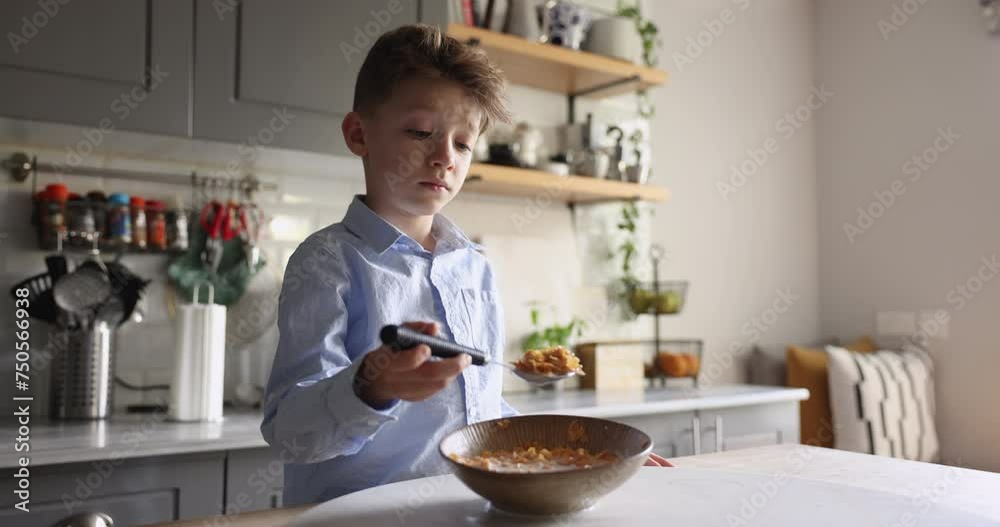 Close up of cute little boy without appetite stand at dining table with bowl of cornflakes in milk, looks dissatisfied, dislike dry sweet breakfast, refuse to eat delicious organic cereals with milk Close up of cute little boy without appetite stand at dining table with bowl of cornflakes in milk, looks dissatisfied, dislike dry sweet breakfast, refuse to eat delicious organic cereals with milk