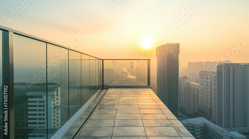 Empty balcony with glass parapet over modern cityscape and sunrise above buildings.