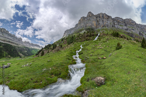 Lush greenery and a vibrant mountain stream cascade down the rocky landscape of Valle de Ordesa, located in the Ordesa y Monte Perdido National Park