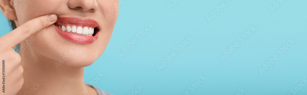 Fototapeta premium Woman showing her clean teeth on light blue background, closeup. Banner design with space for text