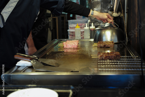 Many pieces of Wagyu meat fried on the pan in the kitchen with hand of chef in background