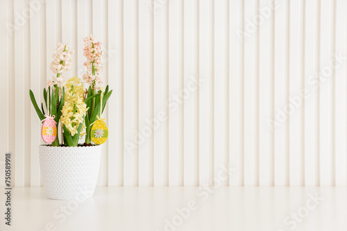 Pot of hyacinths decorated Easter wooden egg toys on white background. Easter celebration concept. Copy space. Front view