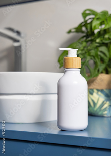 White soap dispenser near basin and green monstera in blue and grey bathroom, close up, mockup photo
