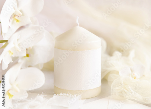 Pillar candle with a blank label near white orchid flowers close up  pastel romantic mockup