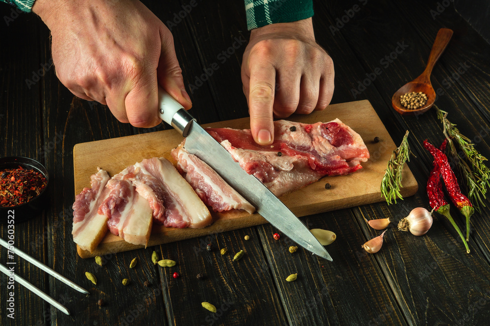 The chef hands use a knife to cut lard or pork belly on a kitchen board before preparing it for dinner. The concept of preparing a hearty and fatty dish