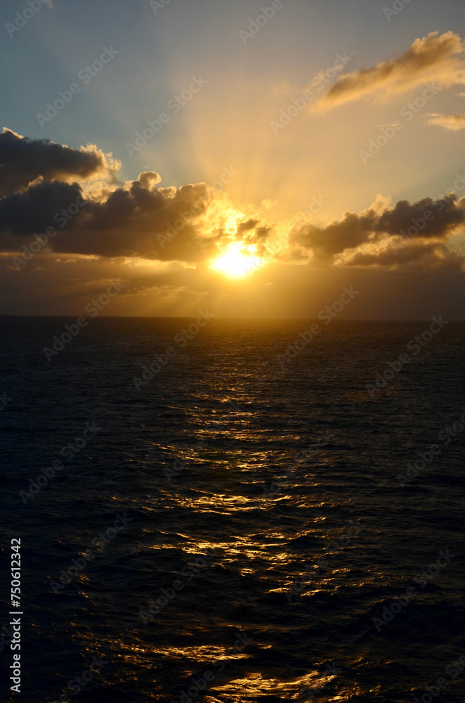 Golden sunset at sea, reflections on water surface, cloudy sky with sunset light sunrays