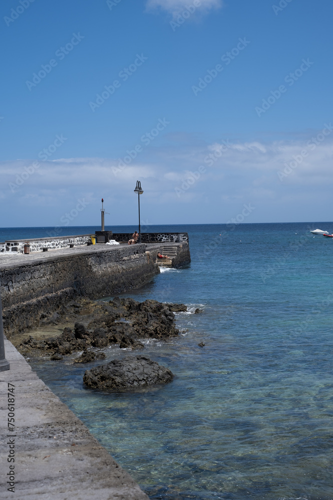 Seascape. Dock of the village of Arrieta with group of boats anchored near the dock in the background. Turquoise Atlantic Ocean. Big white clouds. Village of Arrieta. Lanzarote, Canary Islands, Spain