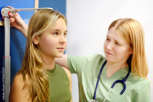 Female doctor measuring of teenage girl height. Schoolgirl patient is at pediatrician appointment. Healthcare for kids. photo